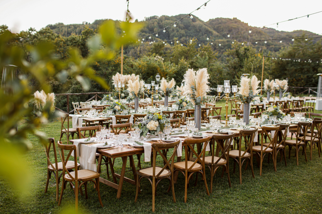 Lange Hochzeitstafeln im Garten mit Pampasgras und Lichterketten