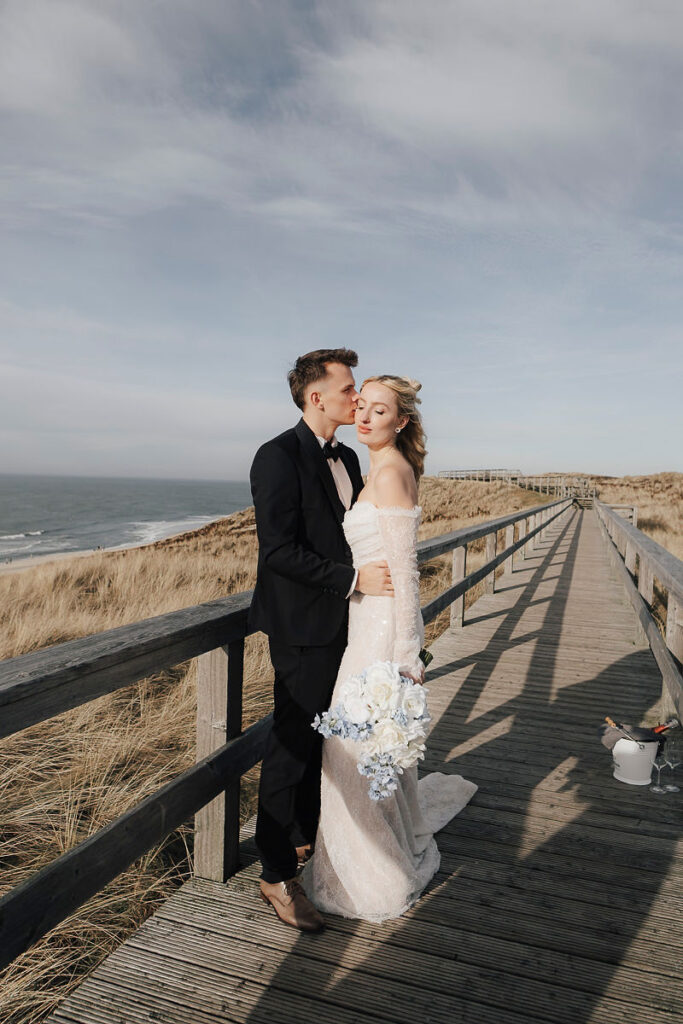 Brautpaar auf dem Bohlenweg durch die Dünen von Sylt, daneben ein Sektkühler