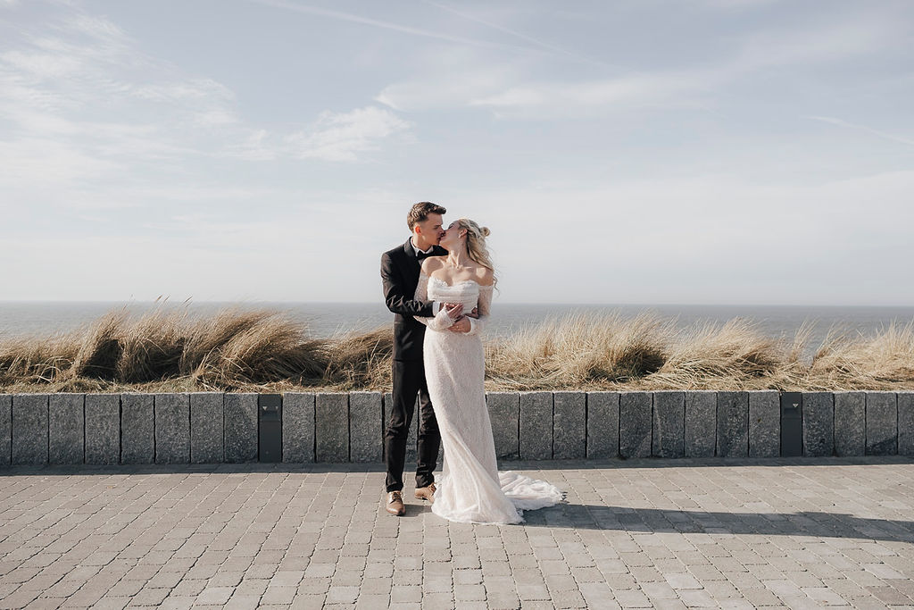 Brautpaar küsst sich auf der Promenade vor den Dünen und dem Meer auf Sylt