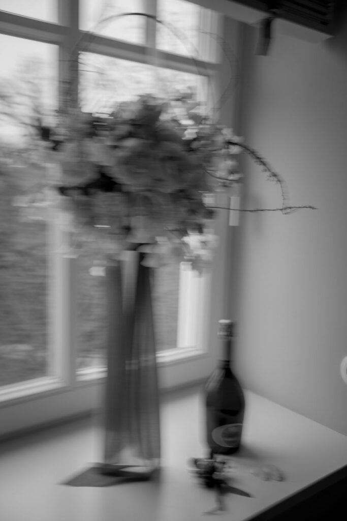 Hoher Brautstrauß in einer Vase am Fenster neben einer Flasche Sekt
