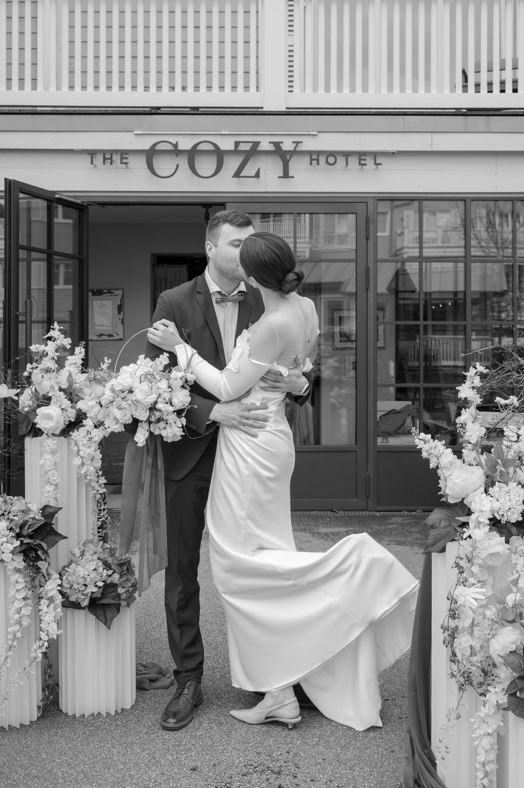 Brautpaar küsst sich zwischen Blumensäulen vor dem Eingang des The Cozy Hotels