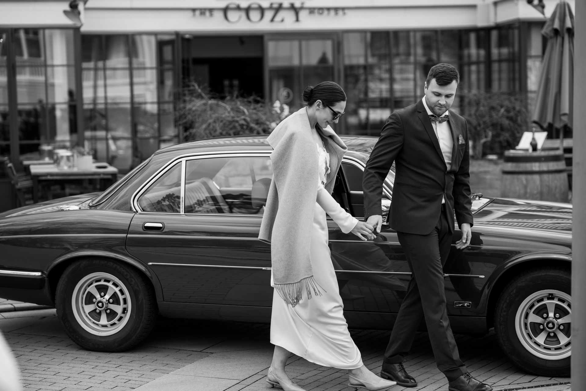 Brautpaar steigt vor dem The Cozy Hotel aus einem Oldtimer als Hochzeitsauto