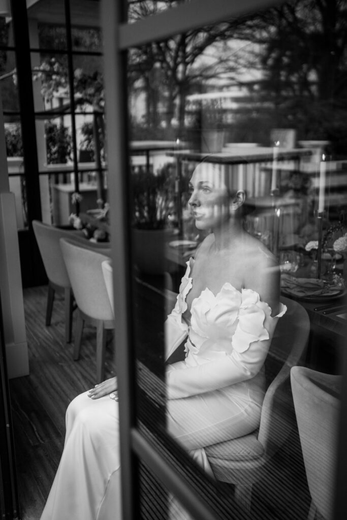 Braut sitzt am gedeckten Tisch, fotografiert durch die Fensterscheibe des Restaurants