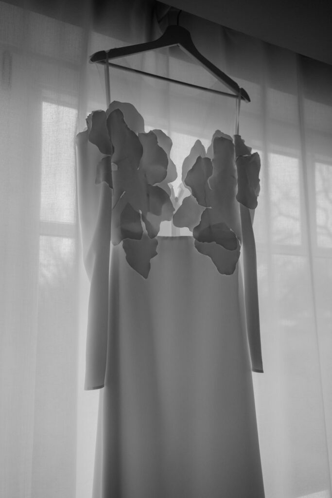 Brautkleid mit Blütenapplikationen hängt vor dem Fenster im Hotelzimmer