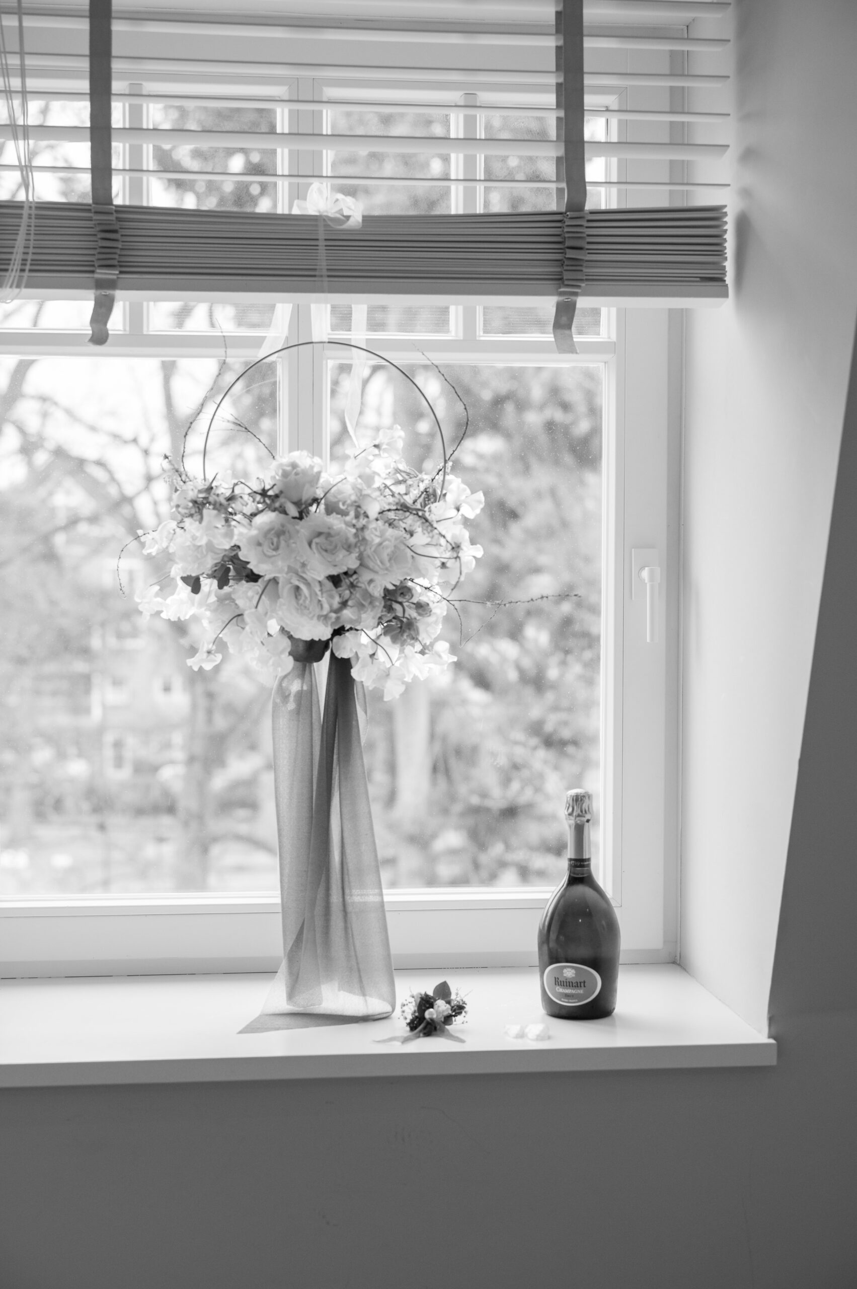 Brautstrauß und Anstecker auf der Fensterbank neben einer Flasche Champagner