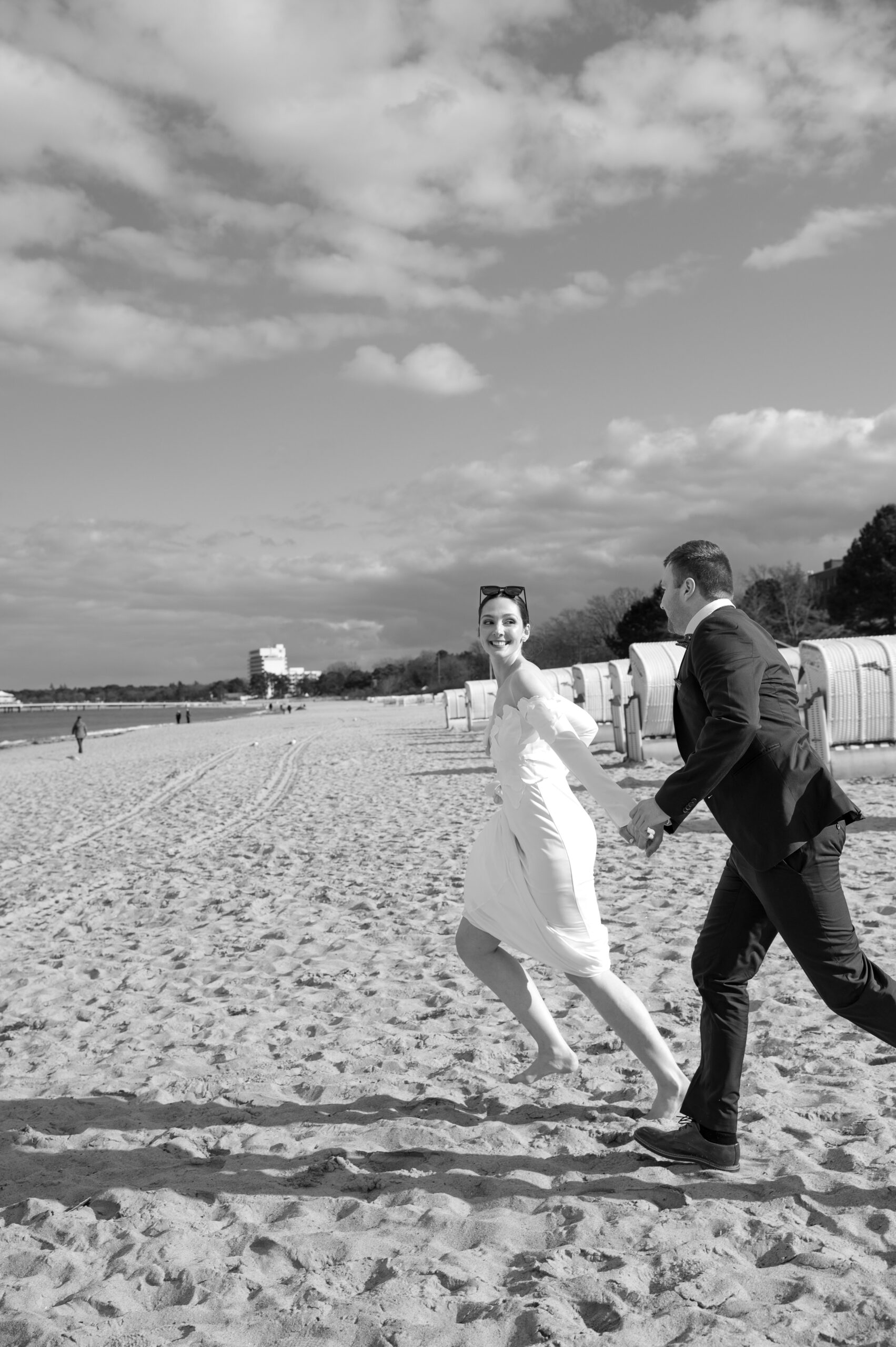 Brautpaar läuft lachend über den Strand an der Ostsee, im Hintergrund Strandkörbe